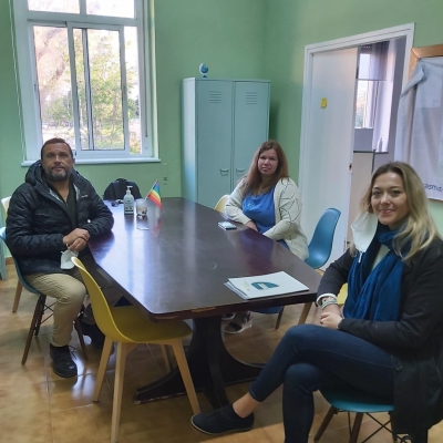 trīs personas sēž pie galda zaļganā telpā