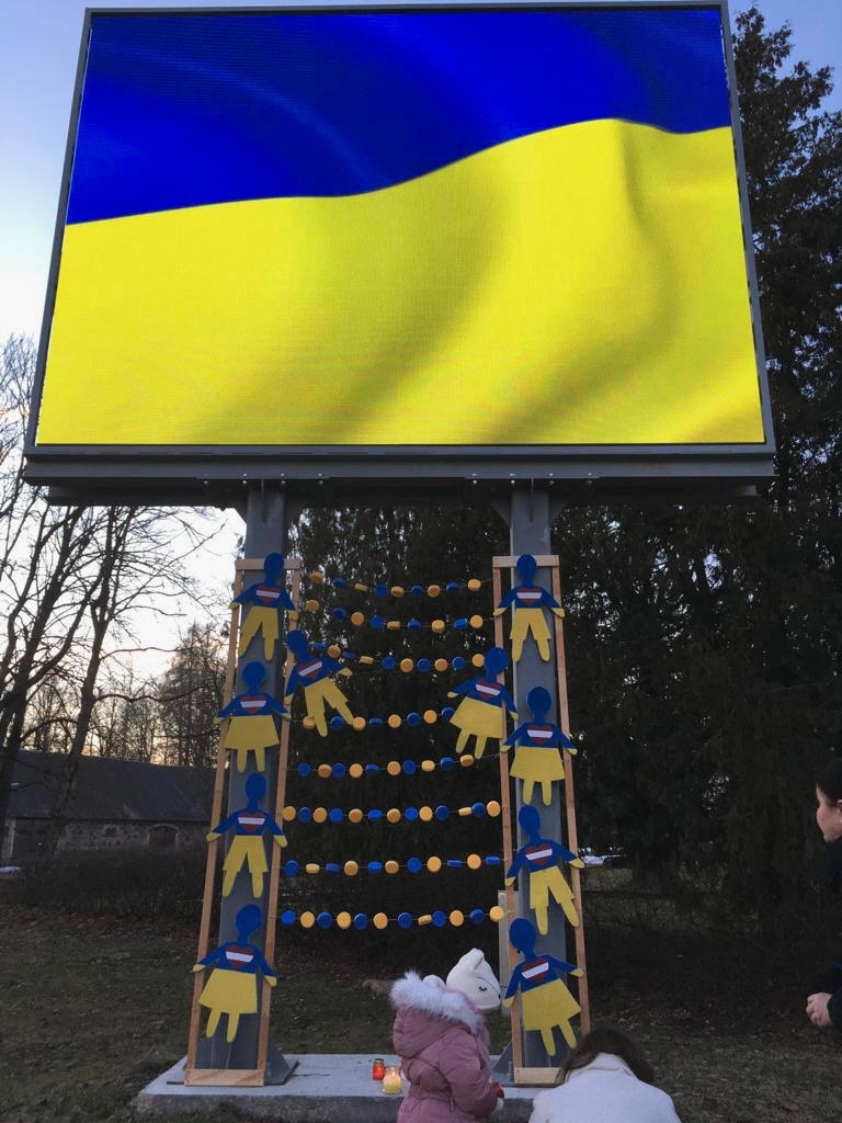 Zasas āra ekrānā redzams Ukrainas karogs, bet pie tā pamatnes pielikti bērnu radītie darbi Ukrainas atbalstam