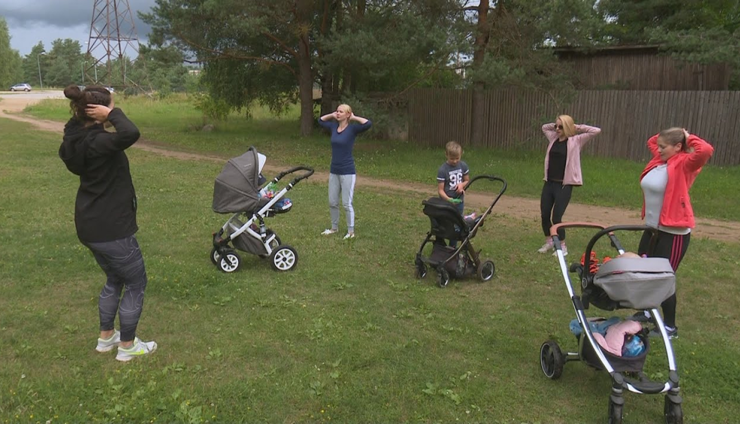 Māmiņas stāv zālājā un vingro, stāvot blakus bērnu ratiņiem