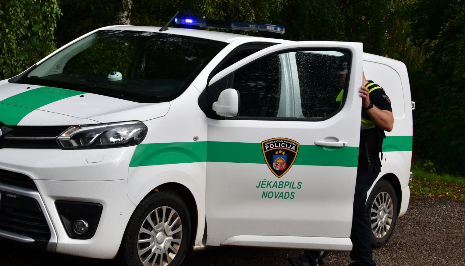 Pašvaldības policijas darbinieks kāpj policijas auto