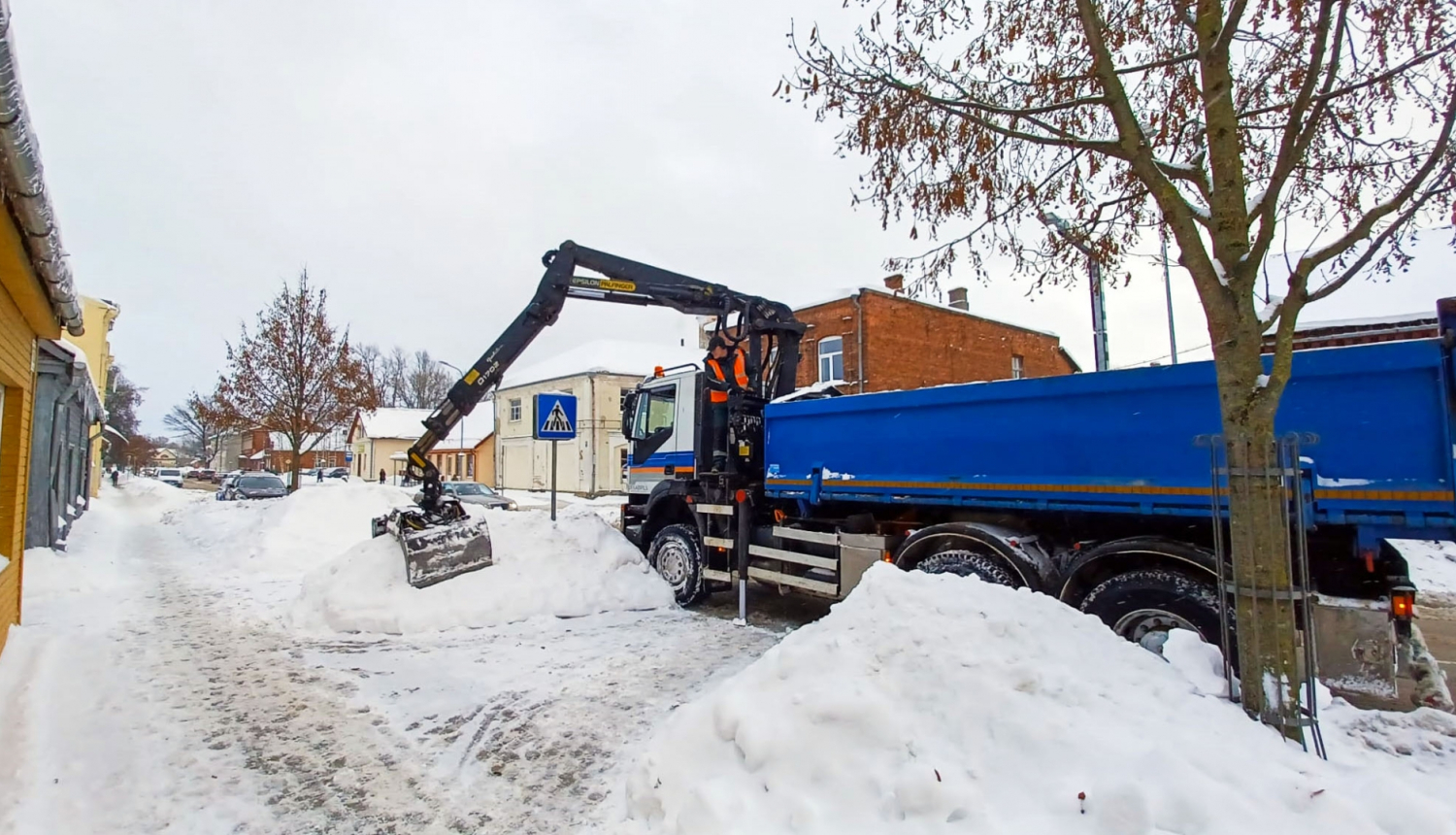 Sniega kaudžu pārkraušana no ietvju malām smagajā transportā