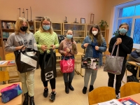 Skolēni stāv klases telpā, turot rokās katrs savu maisiņu vai somu