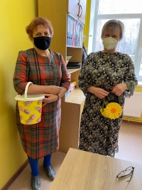 Divas skolotājas stāvot tur rokās traukus, kas tiek izmantoti kā somas