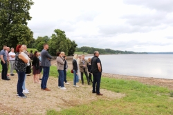 Pašvaldību dalībnieki grupā stāv uz dambja pie Daugavas