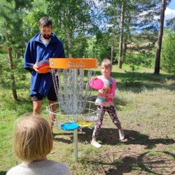 projekta dalībnieki Mežaparkā spēlē disku golfu