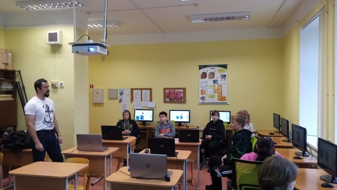 A.Bite (no kreisās) stāv un māca skolēnus, kas sēž klasē pie datoriem