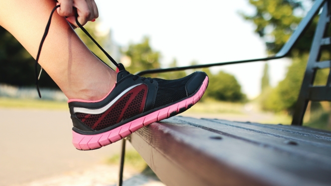 Persona atspiedusi kāju pret soliņu sien rozā sporta kurpei šņores