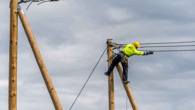 fotogrāfijā redzams elektriķis un elektrības stabi