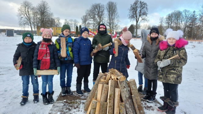 Skolēni stāv pusaplī aiz barikāžu ugunskura, turot rokās pagales