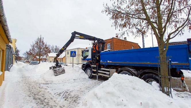 Sniega kaudžu pārkraušana no ietvju malām smagajā transportā