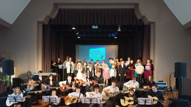 Visi sarīkojuma dalībnieki uzstājas kopā uz skatuves un sēdus uz trepēm