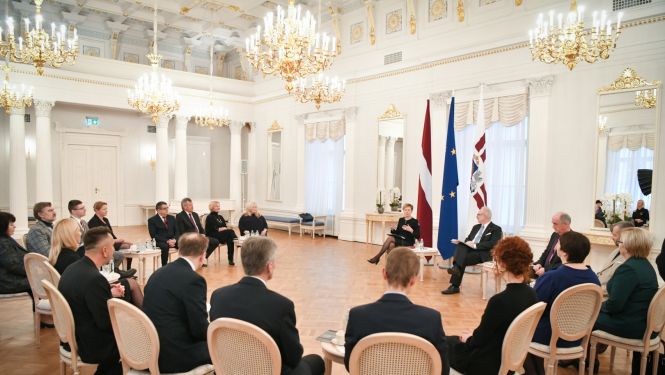 Personas sēž aplī krēslos lielā greznā baltā zālē pie prezidenta