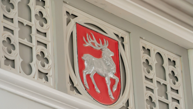 Sēlijas ģerbonis pie baltas koka dekoratīvo elementu sienas