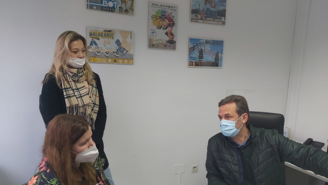 trīs personas telpā ar maskām sarunājas