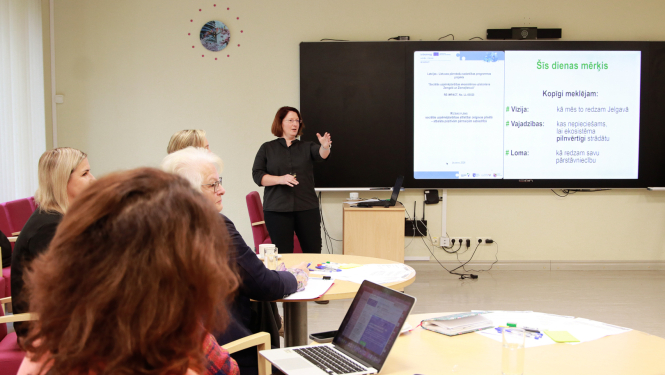 Persona pie digitālās tāfeles stāsta semināra dalībniekiem par projektu