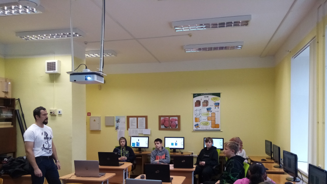 A.Bite (no kreisās) stāv un māca skolēnus, kas sēž klasē pie datoriem