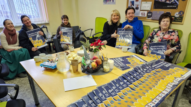 Personas sēž pie galda un tur rokās kalendārus