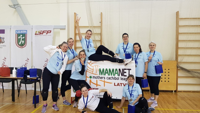 Mamanet komanda sporta zālē pozē kopbildei, turot pa vidu rokās mamanet plakātu