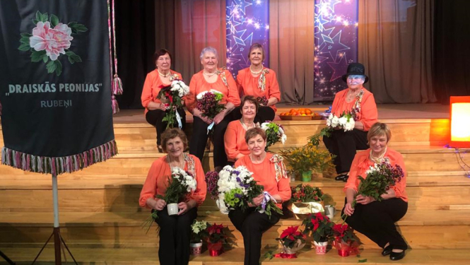 Dāmu deju kopas Draiskās Peonijas dalībnieces sēž uz Rubenes kultūras nama skatuves kāpnēm