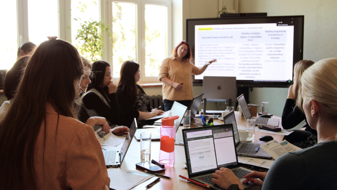 Persona rāda informāciju uz ineraktīvās tāfeles, pārējie telpā skatās uz personu