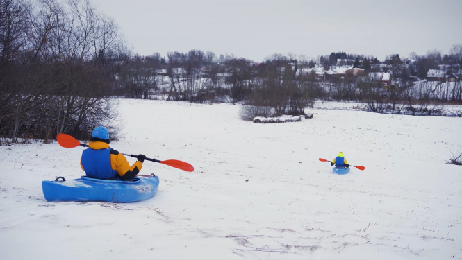 Cilvēki kano laivās šļūc lejup pa sniegotu nogāzi
