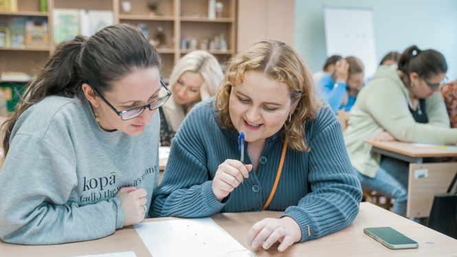 Jaunietes pie galda kopīgi pēta dokumentu