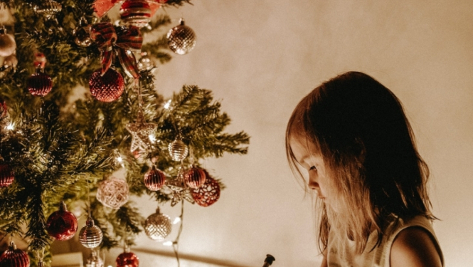 Bērns istabā norūpējies sēž un skatās uz Ziemassvētku eglīti