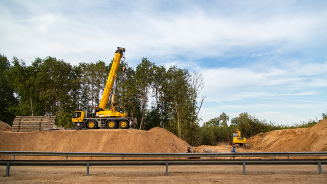 Celtkrāns uz ceļa uzbēruma pie nojaukta tilta, priekšplānā pagaidu apbraucamais ceļš