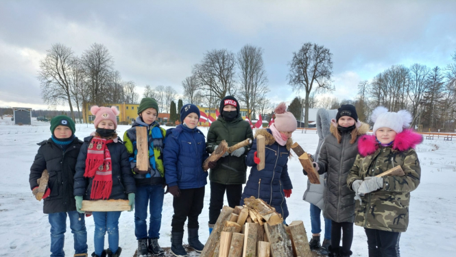 Skolēni stāv pusaplī aiz barikāžu ugunskura, turot rokās pagales