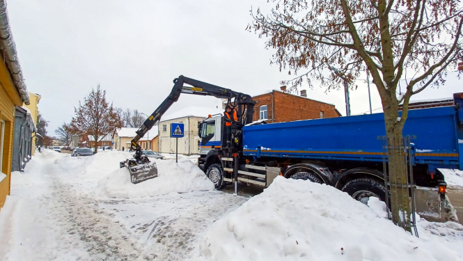 Sniega kaudžu pārkraušana no ietvju malām smagajā transportā