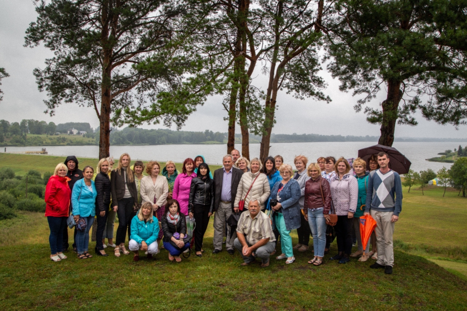 Jēkabpils novada pašvaldības pārstāvji stāv kopbildei pilskalna galā, fonā ezers