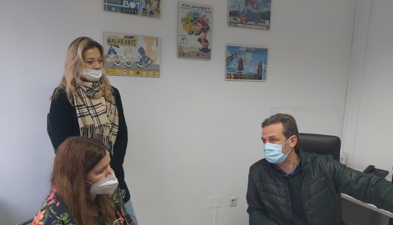 trīs personas telpā ar maskām sarunājas