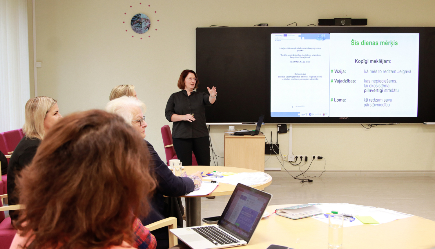 Persona pie digitālās tāfeles stāsta semināra dalībniekiem par projektu