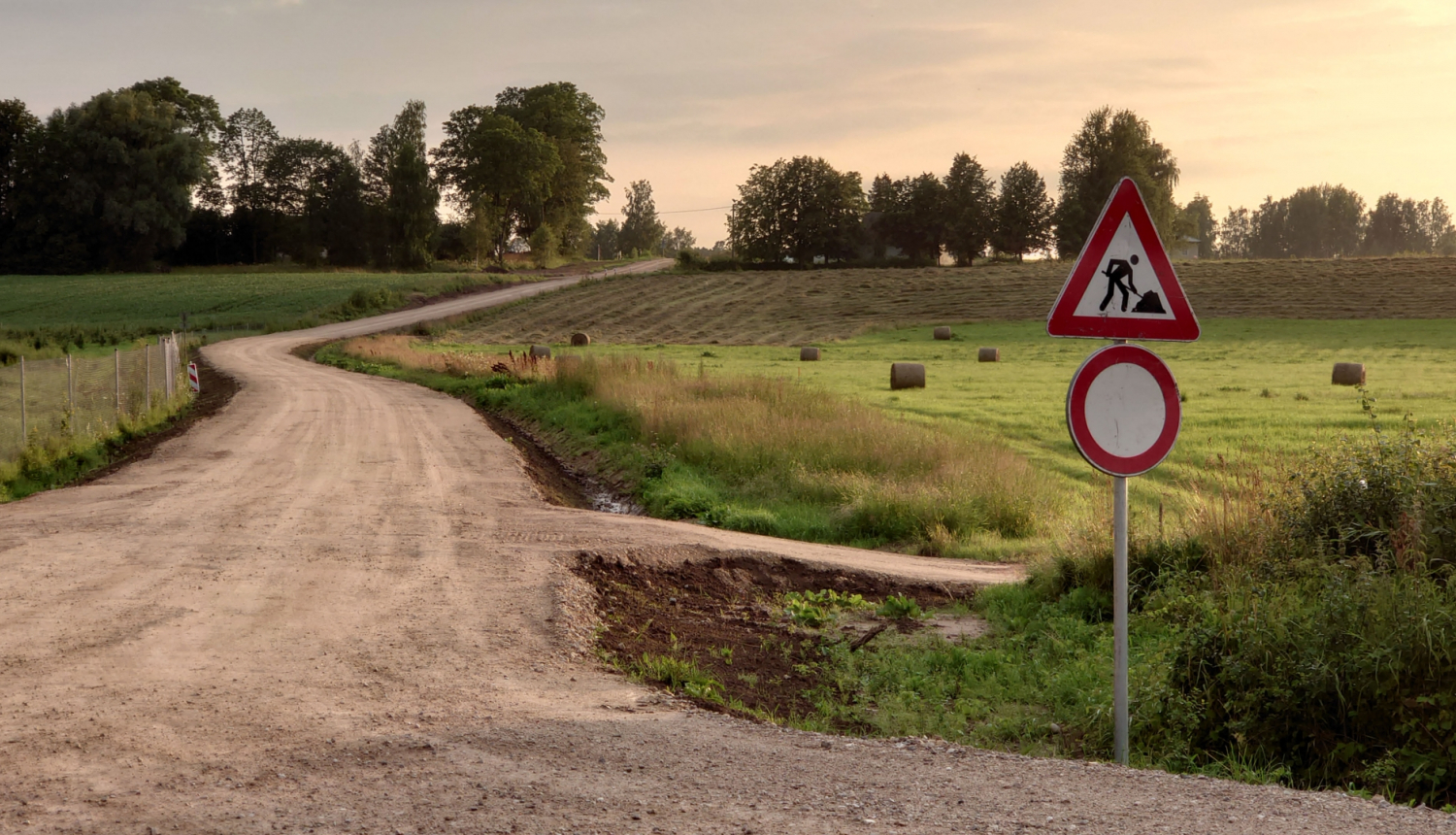 Grants ceļa remontdarbi, tālumā pakalns ar zālāju un ruloniem