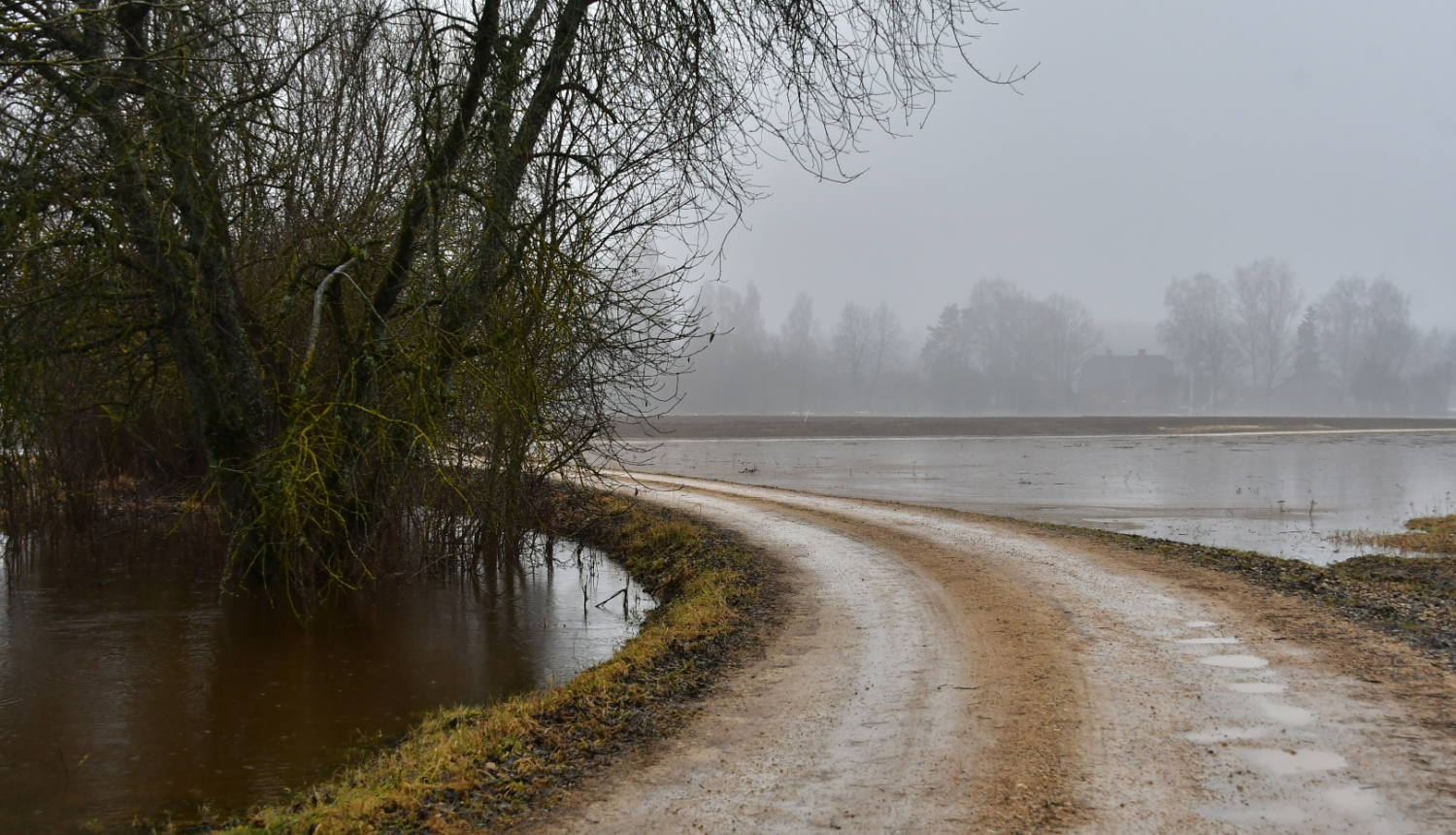 Slapjš zemes ceļš, fonā applūdis lauks