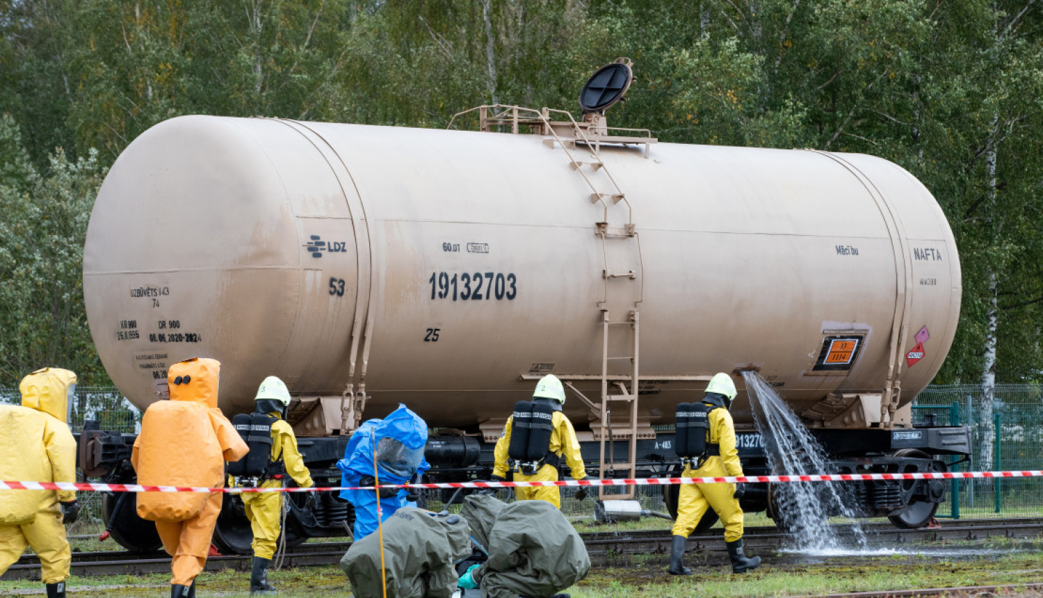 Ugusndzēsēji dzeltenos kostīmos apskata pie sliedēm stāvošu vilciena sastāva škidruma konteineri