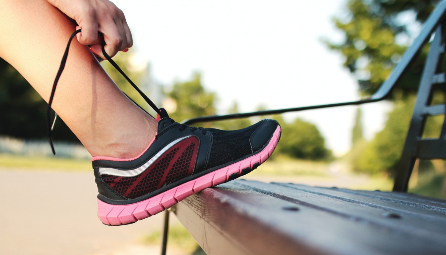 Persona atspiedusi kāju pret soliņu sien rozā sporta kurpei šņores