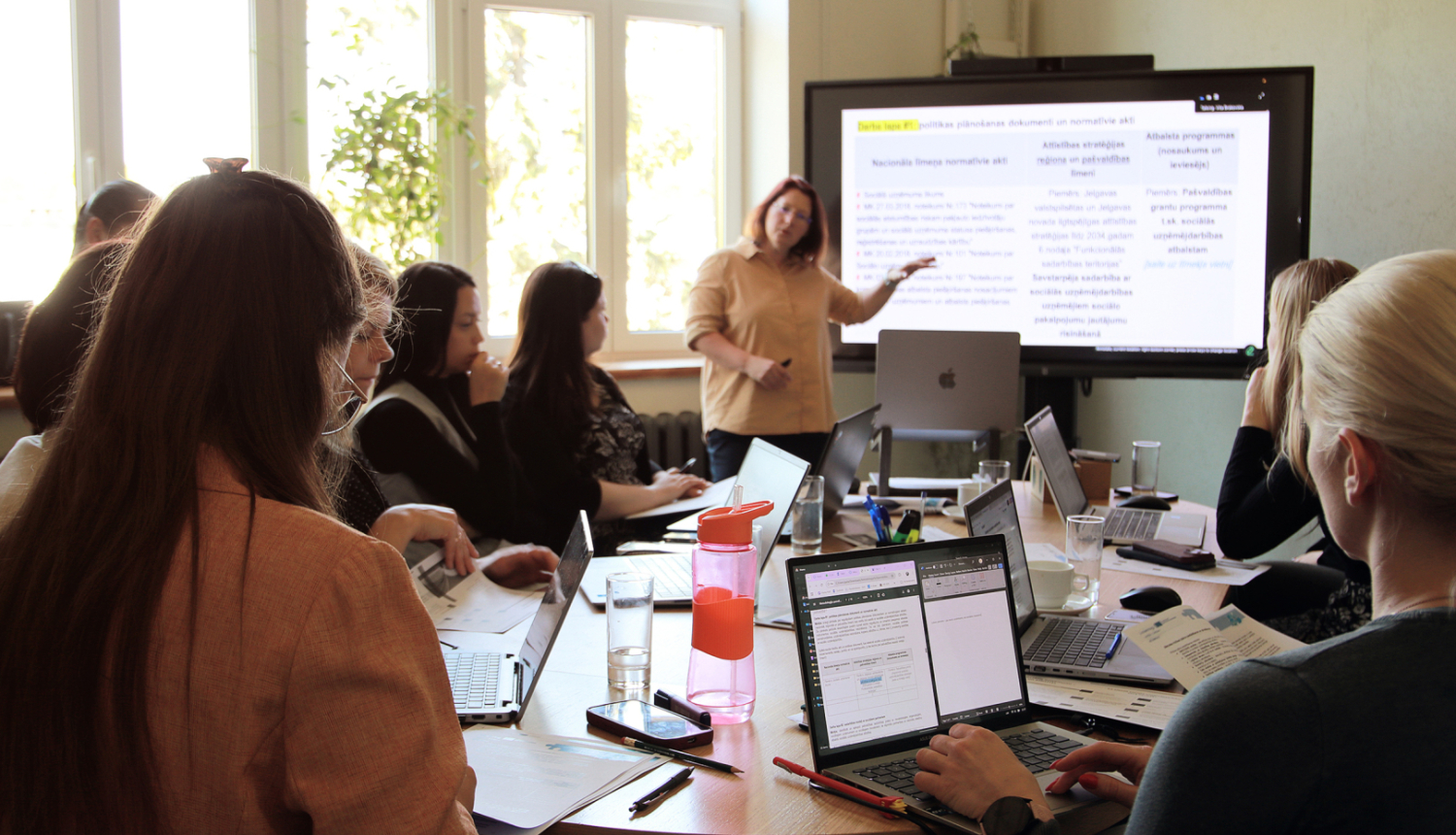 Persona rāda informāciju uz ineraktīvās tāfeles, pārējie telpā skatās uz personu