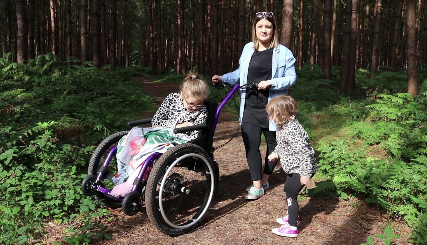 Pieaugušais stumj bērnu ratiņkrēslā pa meža taku