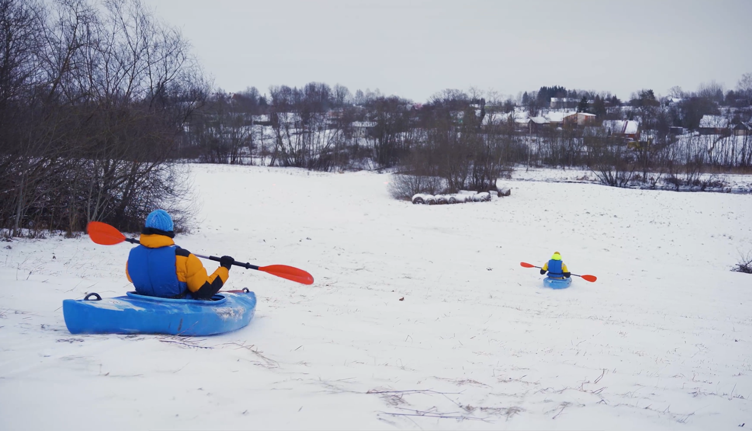 Cilvēki kano laivās šļūc lejup pa sniegotu nogāzi