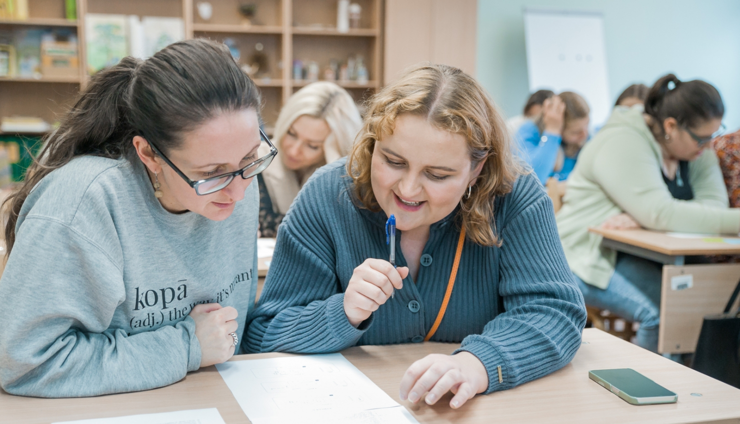 Jaunietes pie galda kopīgi pēta dokumentu