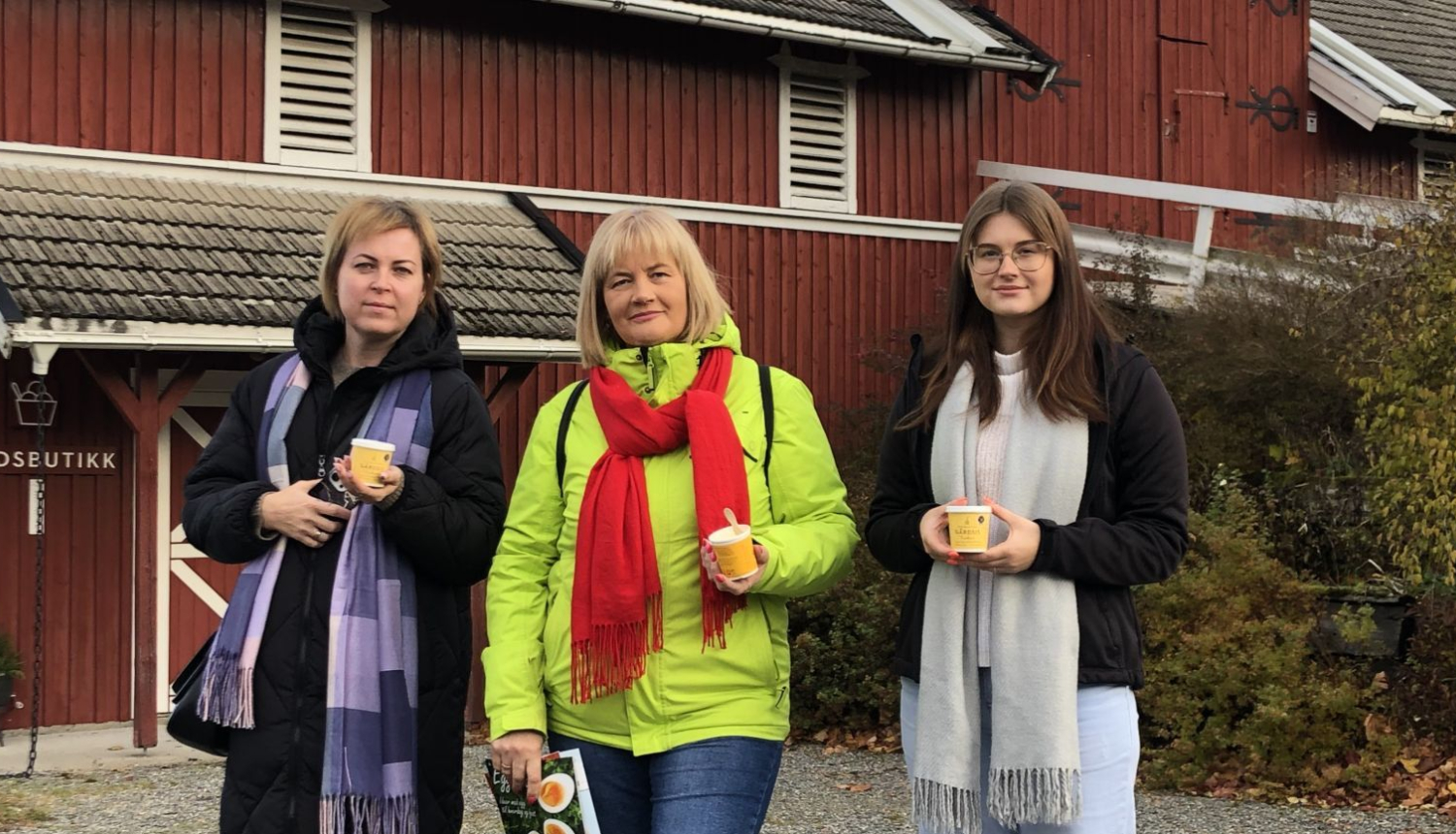 # personas stāv priekšā sarkanam skandināvu tipa namiņam