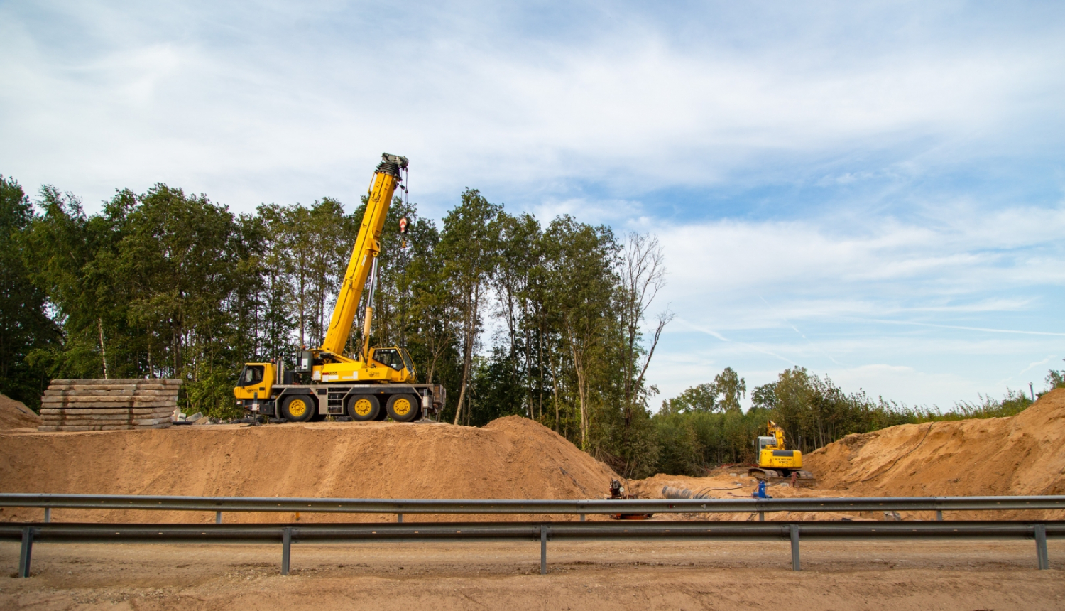 Celtkrāns uz ceļa uzbēruma pie nojaukta tilta, priekšplānā pagaidu apbraucamais ceļš