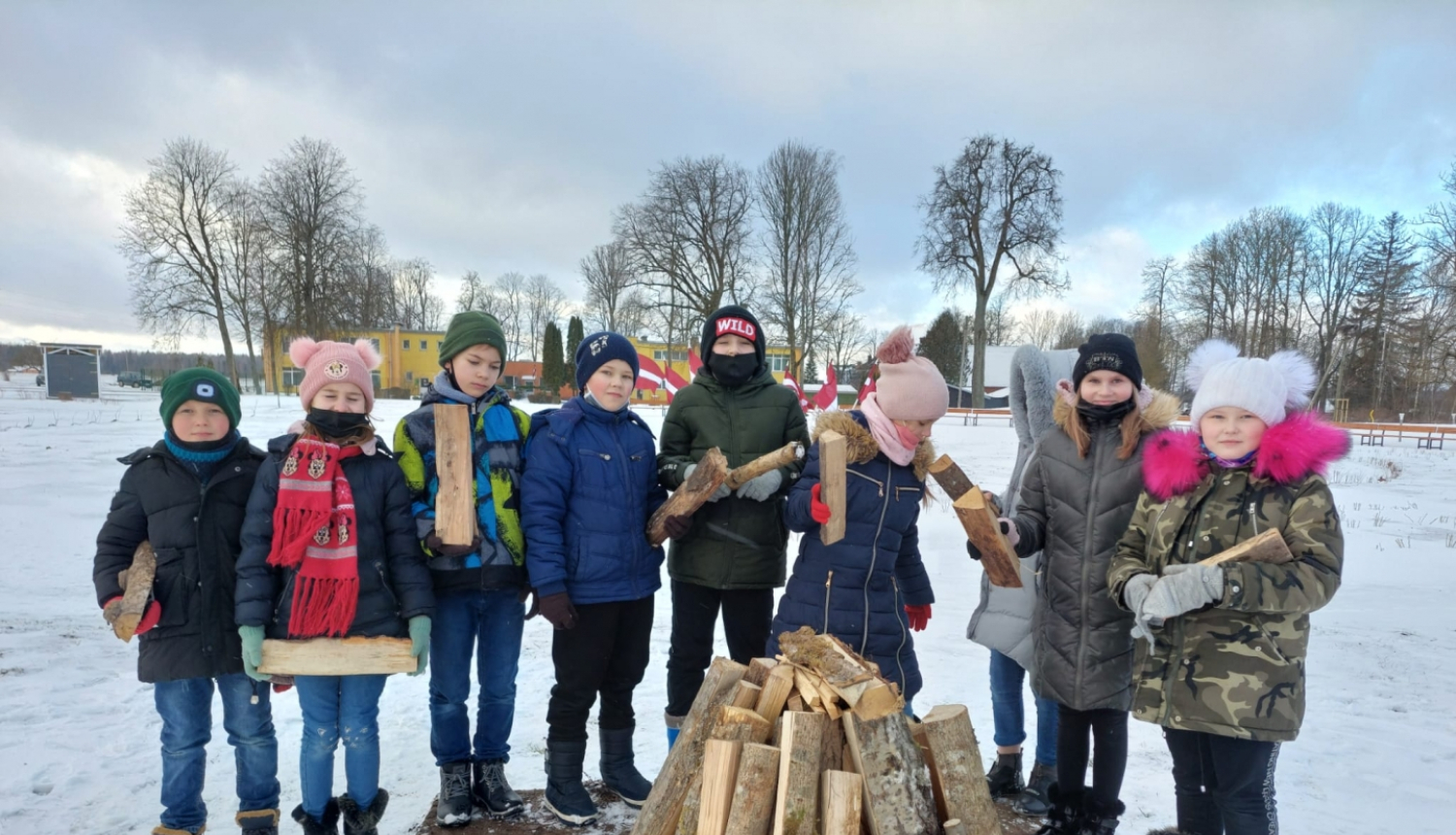 Skolēni stāv pusaplī aiz barikāžu ugunskura, turot rokās pagales