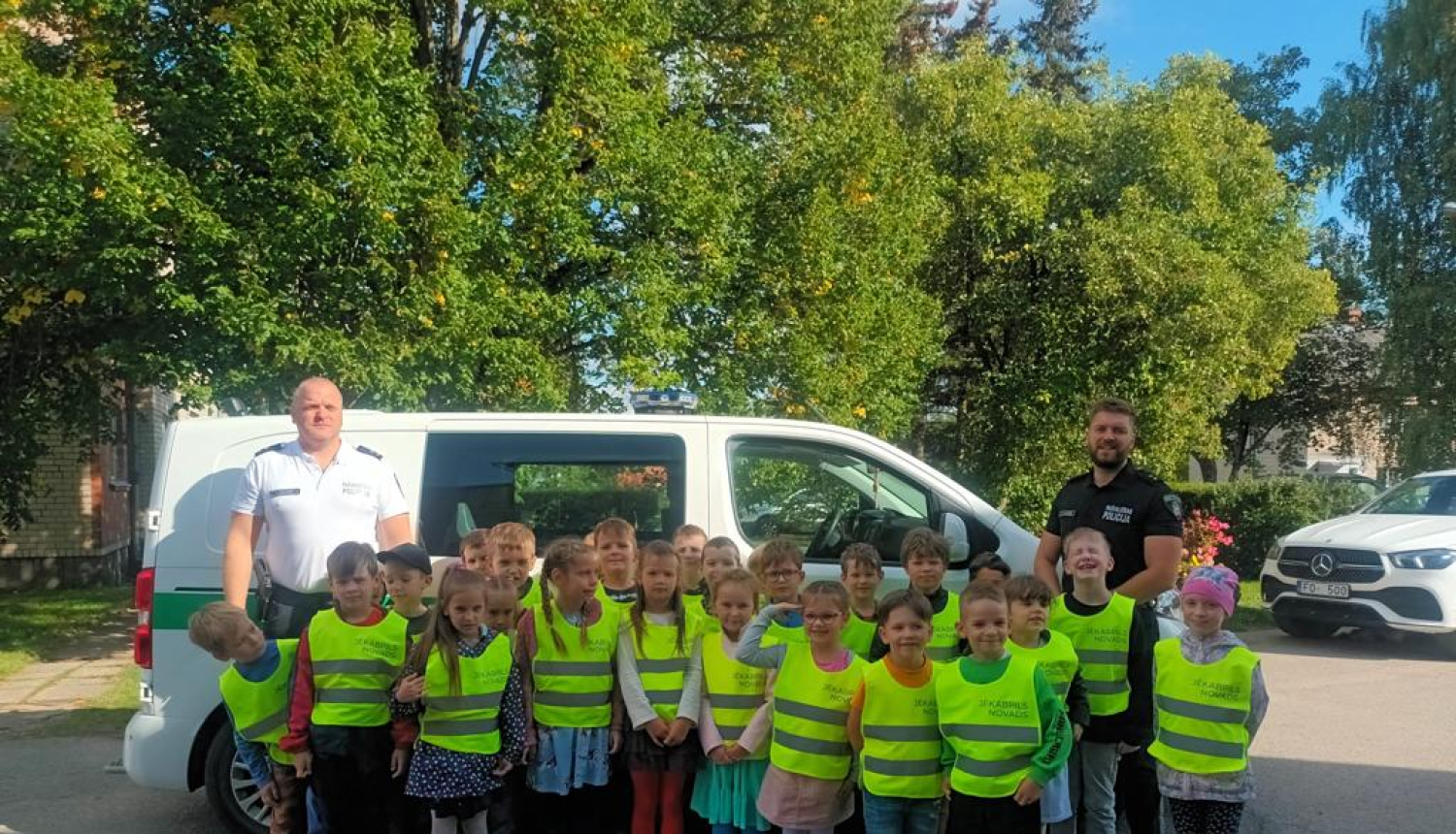 Pašvaldības policijas pārstāvji ar skolēniem pie policijas auto