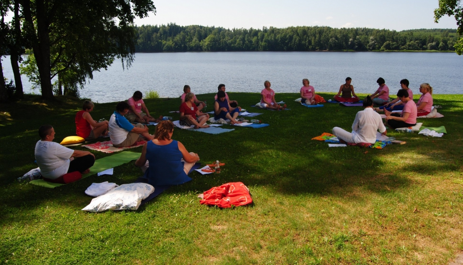 Personas sēž zālājā ūdens tuvumā