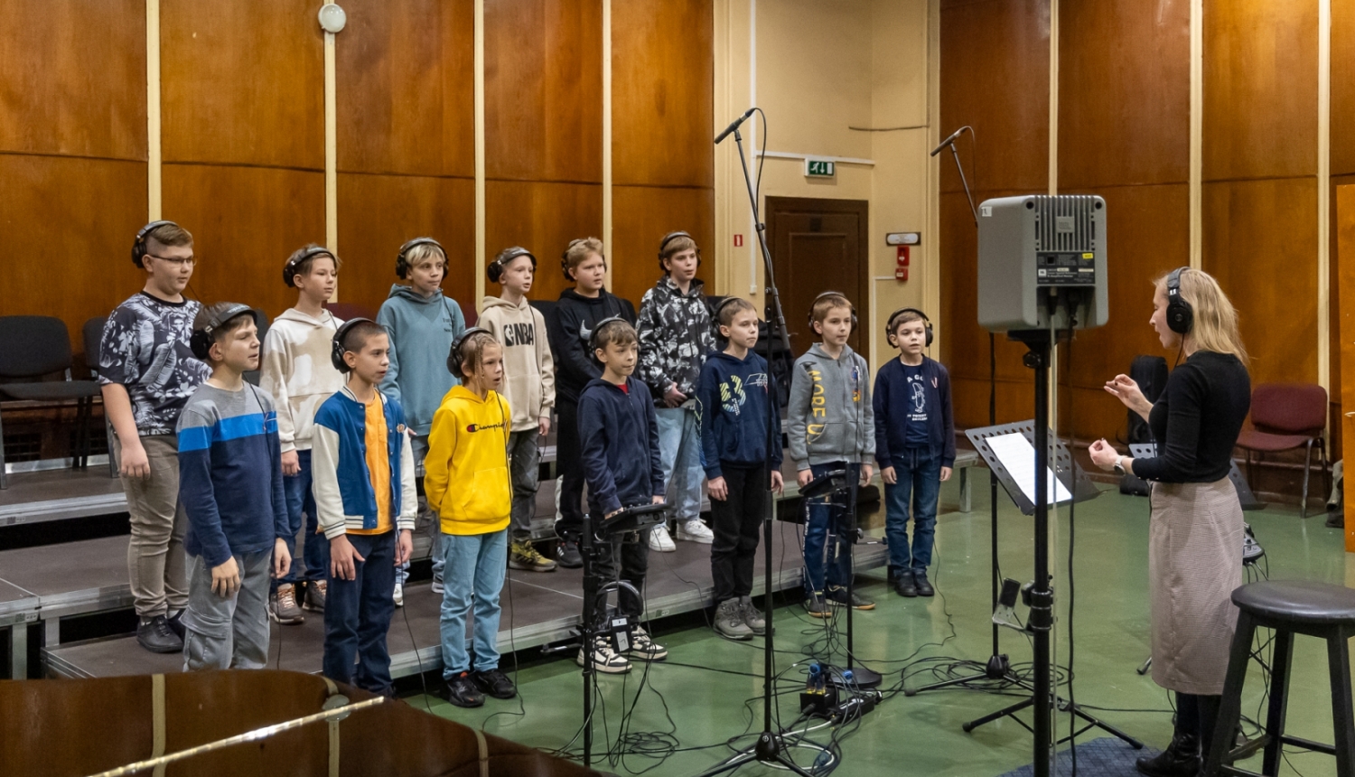 Zēnu koris sastājušies dzied un sieviete diriģē