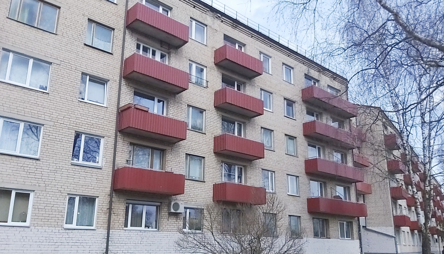 Pelēka daudzdzīvokļi māja ar tumši sarkaniem balkoniem