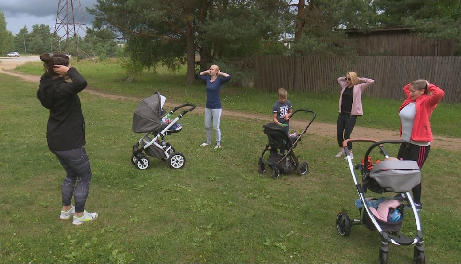 Māmiņas stāv zālājā un vingro, stāvot blakus bērnu ratiņiem