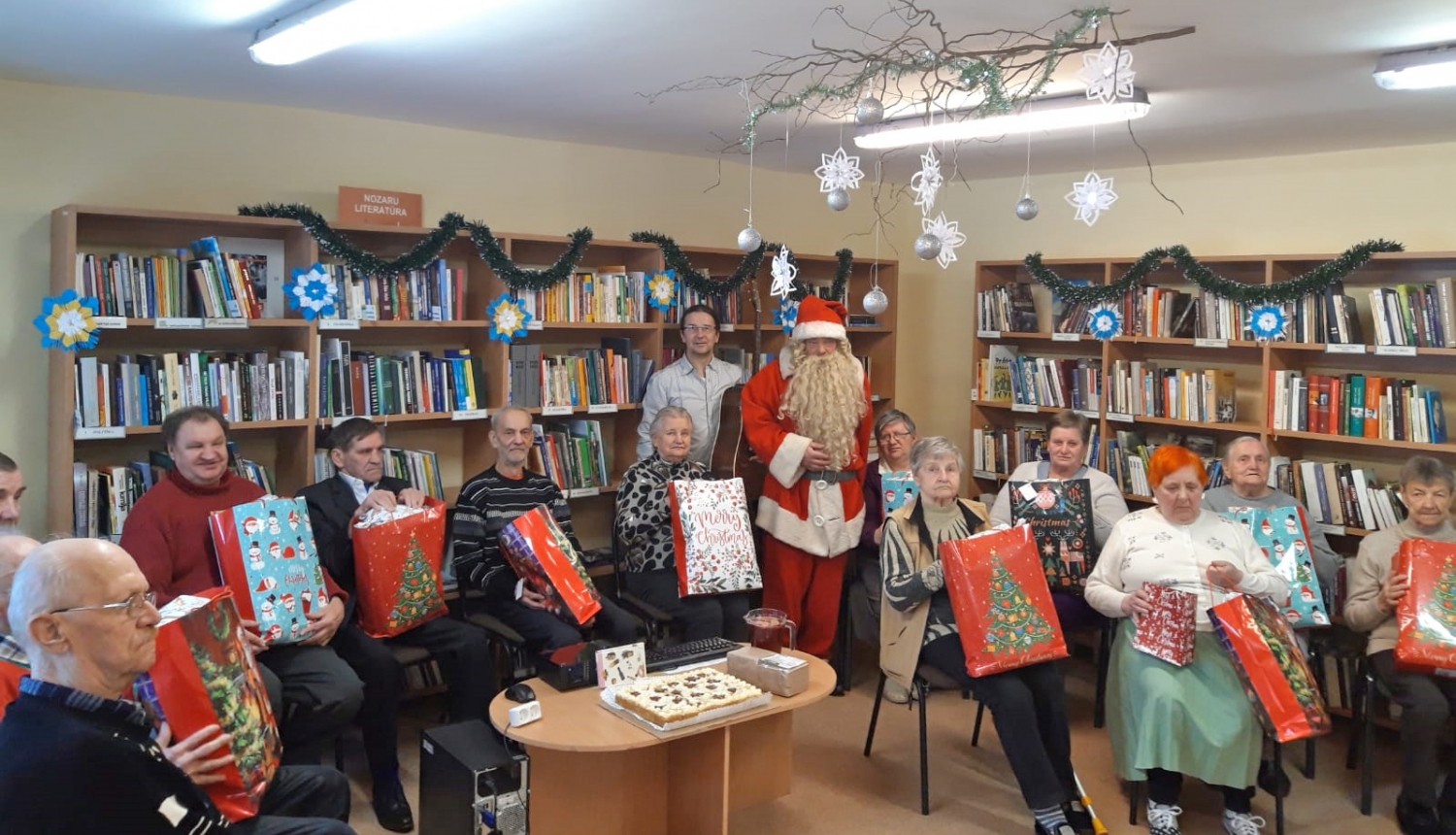 Pansijas Mežvijas iemītnieki ar saņemtajām Ziemassvētku dāvanām klēpī; centrā stāv muzikants Arnis Čakstiņš un Ziemassvētku vecītis